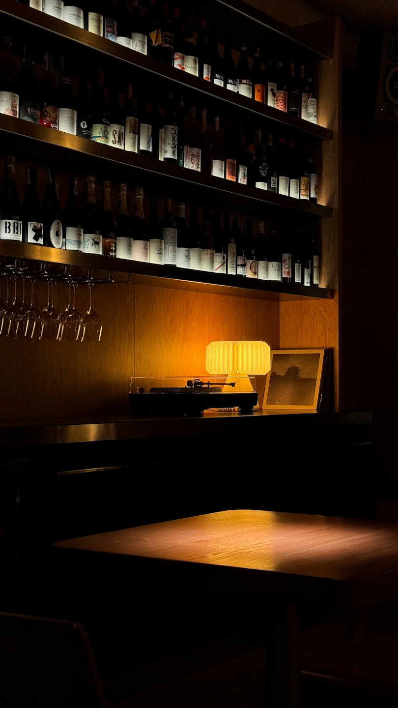 Wine bottles and spirits displayed on wooden shelves in a cozy bar.